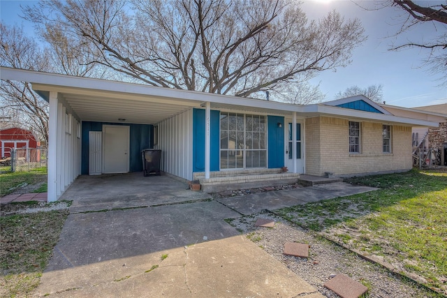 view of front facade featuring fence, an attached carport, concrete driveway, and brick siding