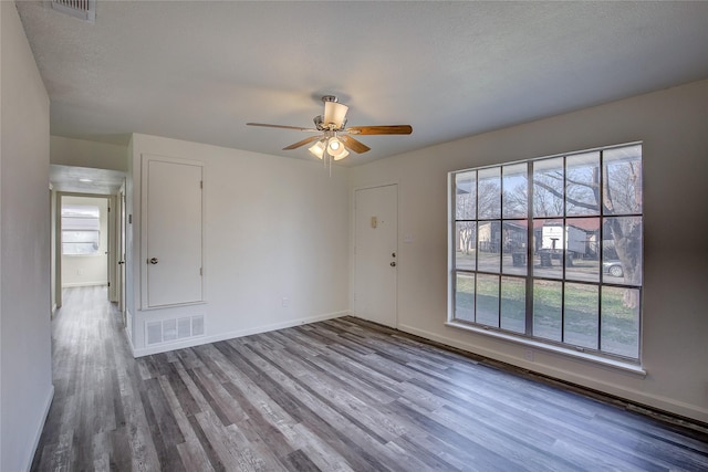 empty room featuring plenty of natural light, wood finished floors, and visible vents