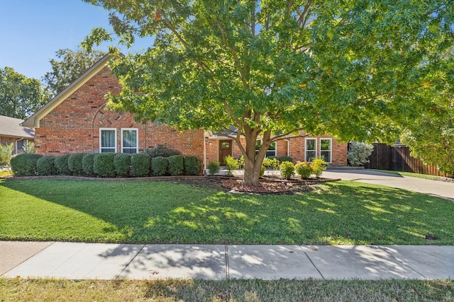 view of property hidden behind natural elements with a front lawn, fence, brick siding, and driveway