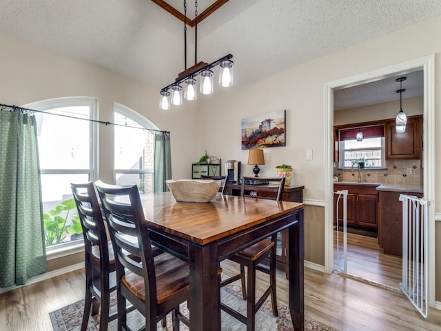 dining room featuring light wood-style floors, baseboards, vaulted ceiling, and a textured ceiling