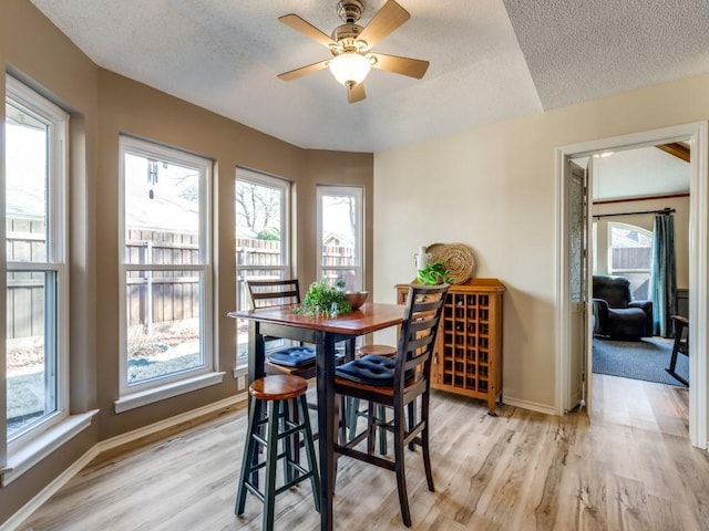 dining space featuring baseboards, light wood-style flooring, and a textured ceiling