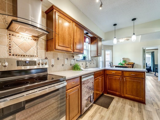 kitchen with appliances with stainless steel finishes, brown cabinetry, light wood-type flooring, a peninsula, and wall chimney exhaust hood