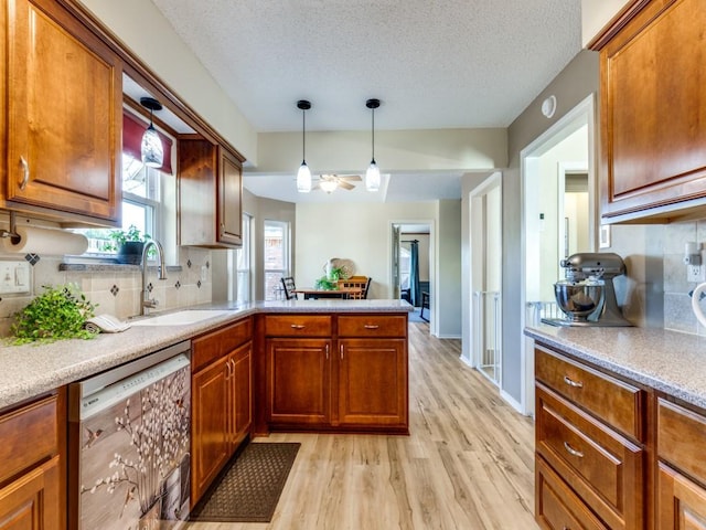 kitchen featuring dishwashing machine, a peninsula, hanging light fixtures, light wood-type flooring, and a sink