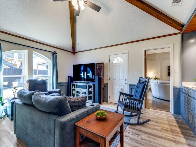 living area featuring light wood finished floors, visible vents, wainscoting, lofted ceiling with beams, and a textured ceiling