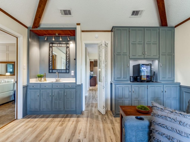 interior space featuring light wood-type flooring, beam ceiling, visible vents, and a sink