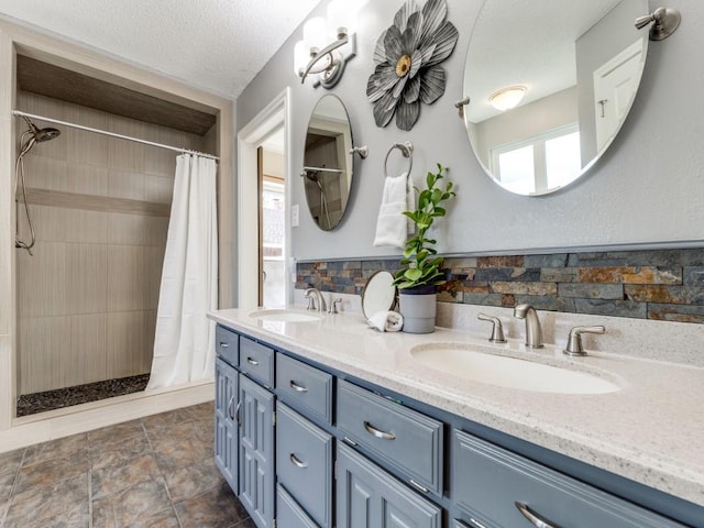 bathroom with double vanity, a textured ceiling, a tile shower, and a sink