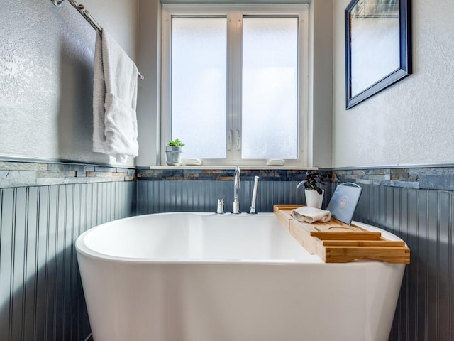 full bathroom featuring a wainscoted wall, a textured wall, a sink, and a soaking tub