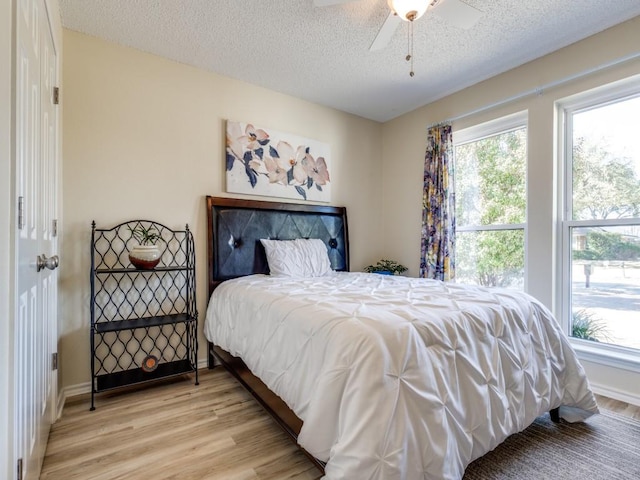 bedroom with light wood-type flooring, multiple windows, a textured ceiling, and baseboards