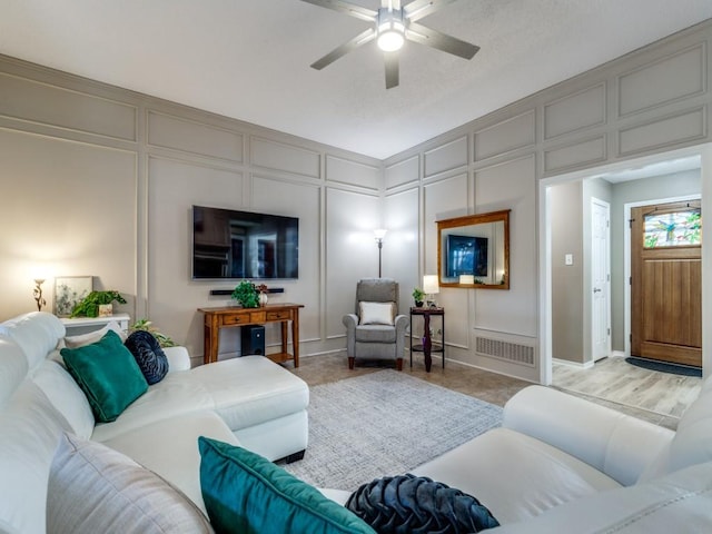 living room with visible vents, a decorative wall, and a ceiling fan