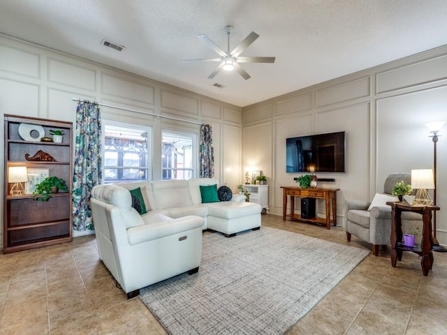 living area featuring light tile patterned floors, visible vents, a decorative wall, and a ceiling fan