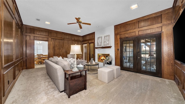 living room with french doors, light carpet, a fireplace, and wood walls