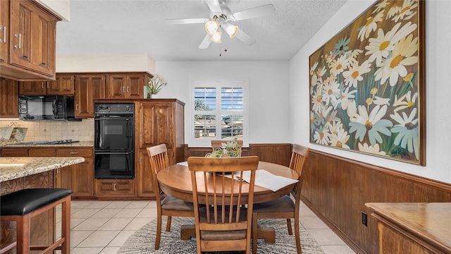 dining area with light tile patterned floors, wood walls, wainscoting, and a textured ceiling