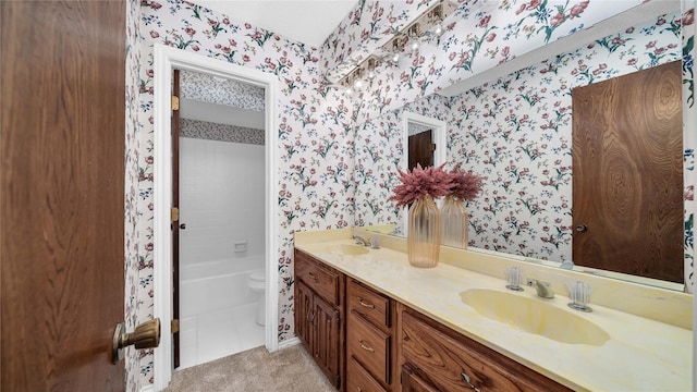 bathroom featuring double vanity, a sink, toilet, and wallpapered walls