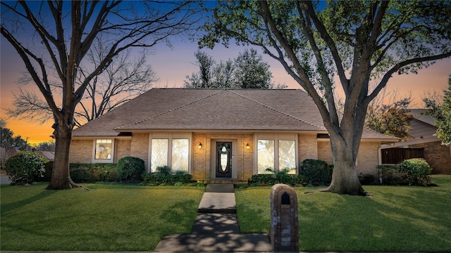 view of front facade featuring a shingled roof, brick siding, and a front lawn