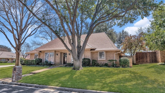 view of front of property featuring roof with shingles, brick siding, a front lawn, and fence