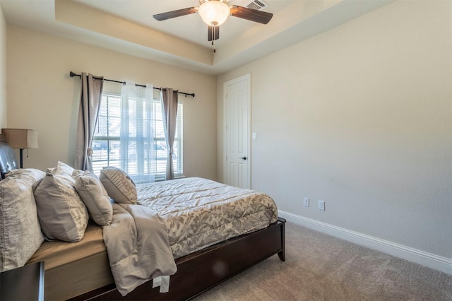 bedroom featuring a tray ceiling, carpet flooring, visible vents, and baseboards