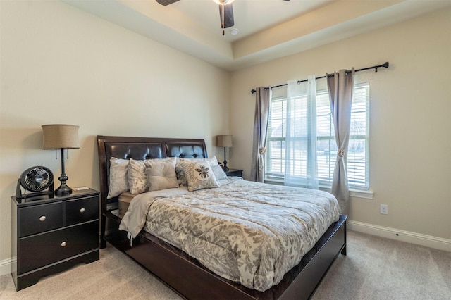 bedroom with light carpet, baseboards, a raised ceiling, and a ceiling fan