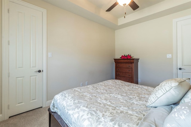 bedroom featuring a tray ceiling, light carpet, and ceiling fan