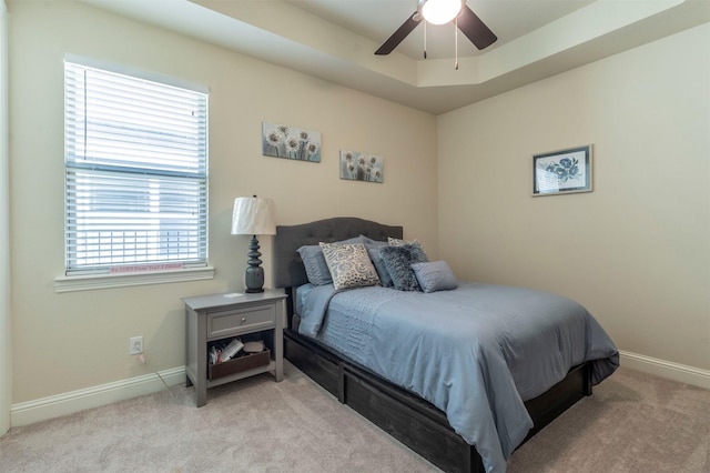 bedroom with a raised ceiling, light colored carpet, ceiling fan, and baseboards