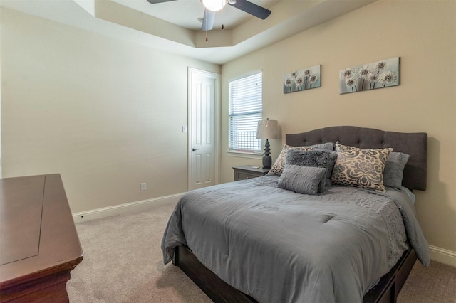 carpeted bedroom featuring a tray ceiling, ceiling fan, and baseboards