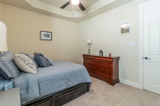 bedroom featuring light carpet, a raised ceiling, a ceiling fan, and baseboards