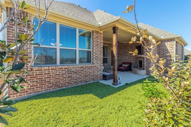 rear view of house with a yard, brick siding, a patio, and a shingled roof