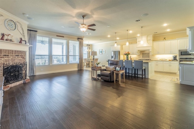 living room with ceiling fan, a brick fireplace, crown molding, and wood finished floors