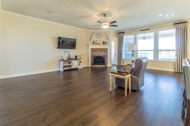 living area featuring ceiling fan, dark wood-type flooring, baseboards, ornamental molding, and a brick fireplace