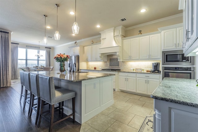 kitchen with visible vents, decorative backsplash, appliances with stainless steel finishes, a breakfast bar, and custom exhaust hood