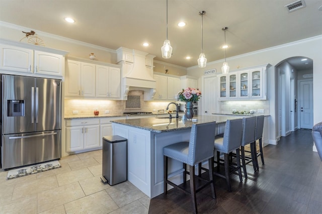 kitchen with stainless steel fridge, visible vents, arched walkways, dark stone counters, and custom exhaust hood