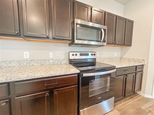 kitchen with light wood finished floors, dark brown cabinets, appliances with stainless steel finishes, and light stone countertops