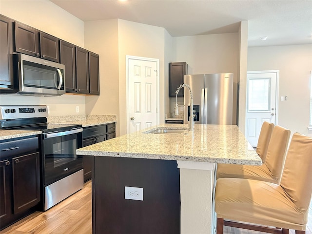 kitchen with a center island with sink, stainless steel appliances, light wood-style floors, a sink, and light stone countertops