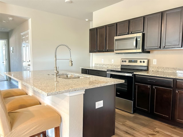 kitchen featuring light stone counters, stainless steel appliances, light wood-style flooring, a sink, and a kitchen bar