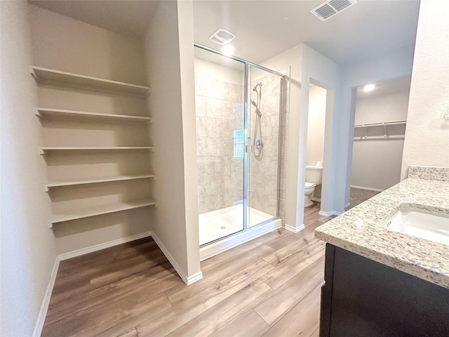 full bath featuring toilet, wood finished floors, visible vents, a spacious closet, and a shower stall