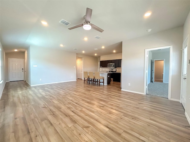 unfurnished living room with recessed lighting, visible vents, light wood-style flooring, a sink, and baseboards