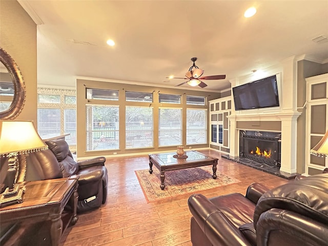 living room with a high end fireplace, ceiling fan, ornamental molding, wood finished floors, and recessed lighting