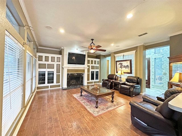 living room featuring visible vents, a ceiling fan, wood finished floors, crown molding, and a fireplace