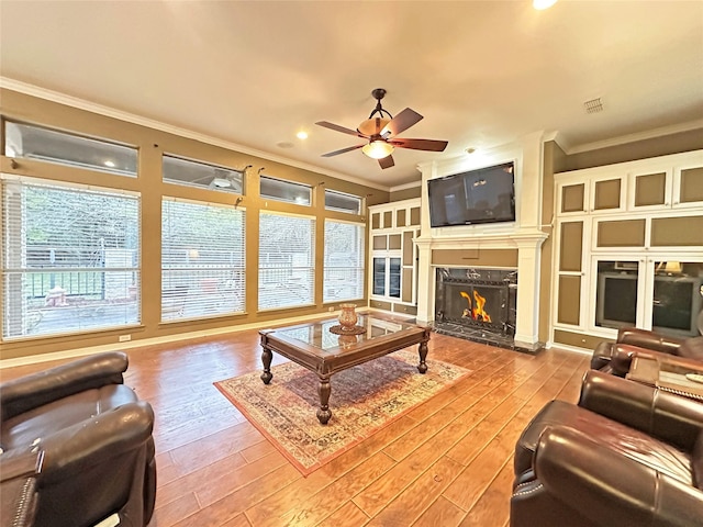 living room featuring visible vents, wood-type flooring, a premium fireplace, ceiling fan, and crown molding