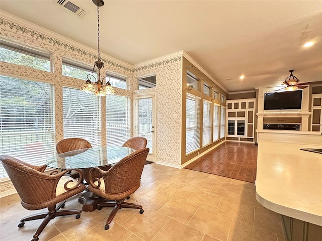 dining area with visible vents, baseboards, ornamental molding, a fireplace, and ceiling fan with notable chandelier