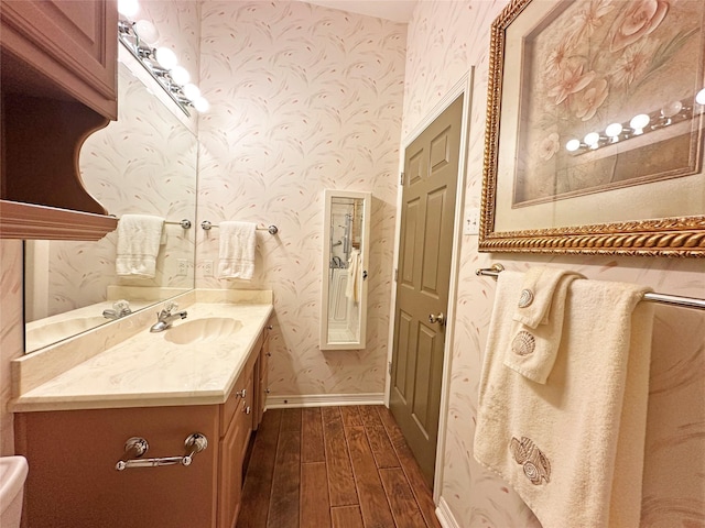 bathroom with baseboards, wood finished floors, vanity, and wallpapered walls