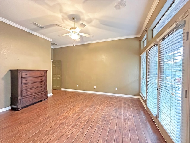 empty room featuring visible vents, ornamental molding, ceiling fan, wood finished floors, and baseboards