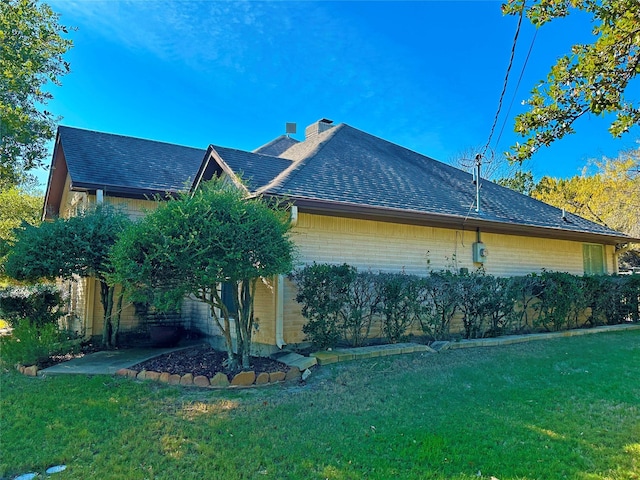 view of home's exterior featuring roof with shingles, brick siding, a lawn, and a chimney