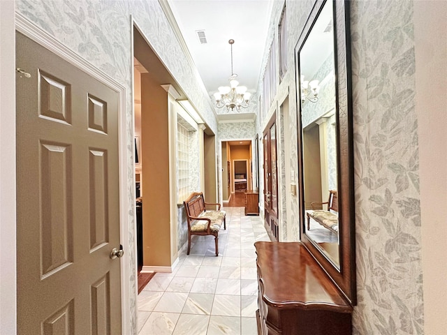 corridor with visible vents, ornamental molding, a chandelier, baseboards, and wallpapered walls