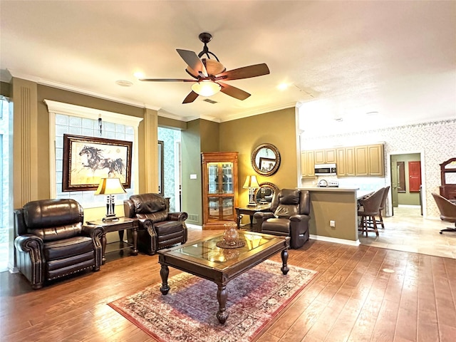 living room with light wood finished floors, wallpapered walls, visible vents, a ceiling fan, and ornamental molding