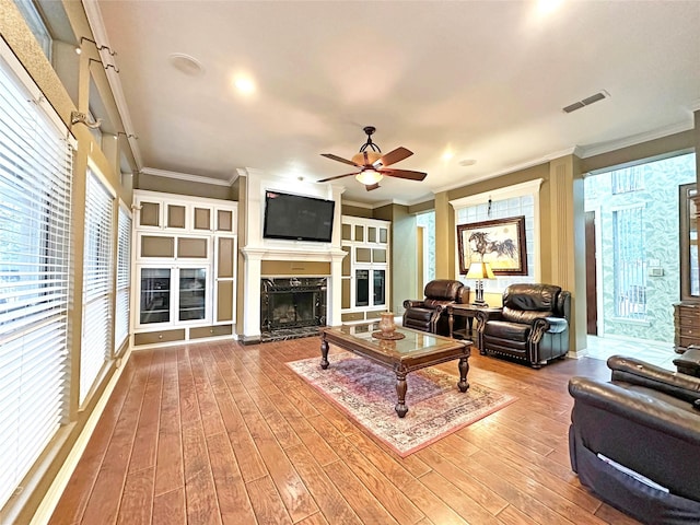 living area featuring ornamental molding, wood-type flooring, a high end fireplace, and visible vents