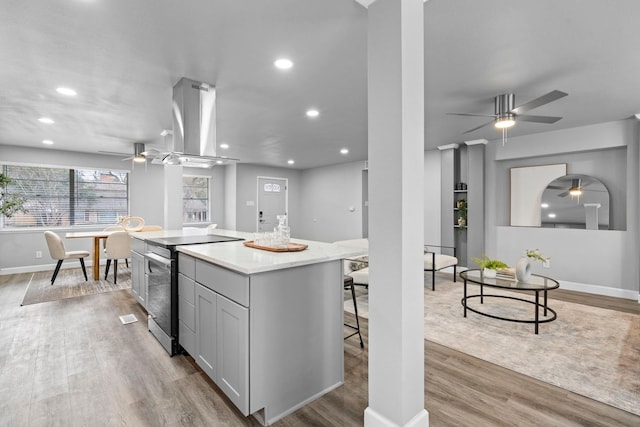 9723 Queenswood Ln, Dallas, TX 75238 - kitchen with a ceiling fan, stainless steel range with electric cooktop, island exhaust hood, light wood-style flooring, and a kitchen island