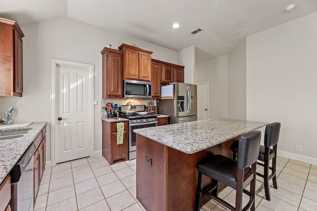 kitchen with light stone counters, stainless steel appliances, tasteful backsplash, visible vents, and a kitchen island