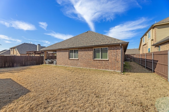 back of property featuring brick siding, a shingled roof, a lawn, a pergola, and a fenced backyard