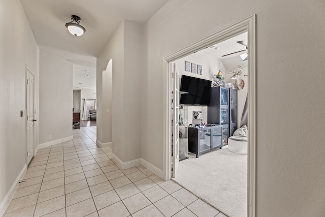 hallway featuring tile patterned flooring, carpet flooring, arched walkways, and baseboards