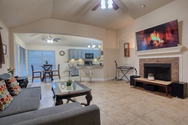 living area featuring light tile patterned floors, arched walkways, lofted ceiling, a fireplace, and ceiling fan with notable chandelier